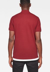 Burgundy pikétröja med krage och korta ärmar. Det strukturerade tyget är mjukt, med en kontrasterande vit nederkant.