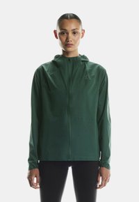 Kerge roheline tõmblukuga jakk kapuutsiga, valminud siledast nailonist. Omab elastseid varrukaid ja minimalistlikku disaini, kus rinnal on logo.