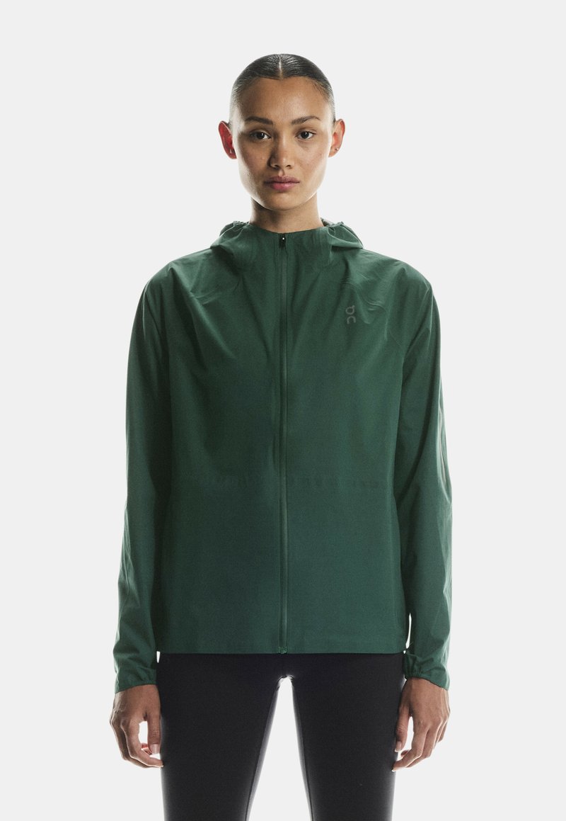 Kerge roheline tõmblukuga jakk kapuutsiga, valminud siledast nailonist. Omab elastseid varrukaid ja minimalistlikku disaini, kus rinnal on logo.