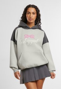 Grå og svart fargeblokkert hettegenser med en frontlomme, prydet med rosa sløyfe og "babygirl" tekst, kombinert med en plisserte grå skjørt.