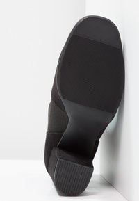 Stivaletto in suede nero con suola in gomma a scanalature orizzontali, tacco spesso e parte superiore in tessuto liscio per un comfort aggiuntivo.