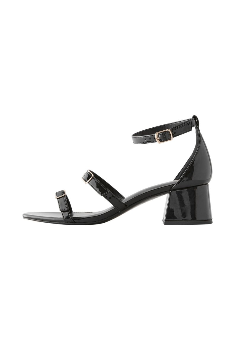Sandale en cuir verni noir avec un talon fermé, une bride à la cheville et deux brides à l'avant. Présente un talon carré bloc et une finition lisse.