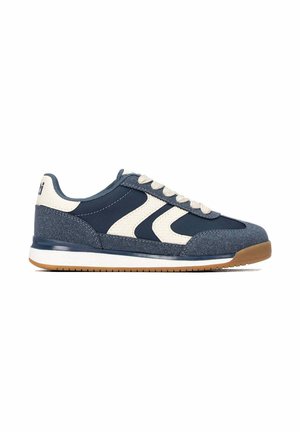 Zapatilla azul marino y blanca con cordones beige, suela texturizada y entresuela blanca, mostrada de perfil sobre fondo blanco.