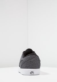 Nike SB-skor med en strukturerad grå stickad överdel, svarta accenter och en vit sula. Bakpå finns en logotagg.