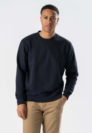 Marineblå sweatshirt lavet af bomuld, rund hals, ribbede manchetter og kant, iført med beige bukser. Struktureret stof, afslappet pasform.