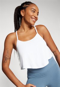 Weißes, kurzes Tanktop mit dünnen Trägern, kombiniert mit hellblauen High-Waist Leggings. Hat eine glatte Textur und einen entspannten Schnitt.