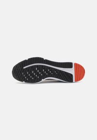 Semelle extérieure en caoutchouc noir avec un motif texturé ; semelle intermédiaire blanche avec un accent rouge au talon et une surface lisse au niveau de l'avant-pied.