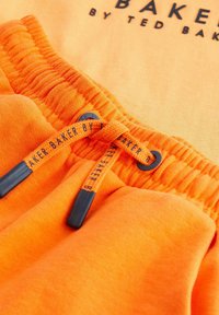 Orange bomuldsshorts med snøre og sorte aglets samt en broderet logo. Blød tekstur med detaljeret syning ved taljen.
