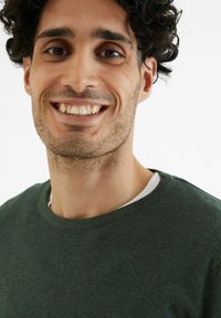 Groene ronde hals trui met een gestructureerd breisel, gedragen over een wit shirt, met een relaxte fit en zichtbare stikseldetails.