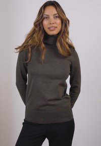 Tamnozeleni turtleneck pulover napravljen od mekog pletiva, s rebrastim donjim rubom i manžetama, osmišljen u uskom kroju.