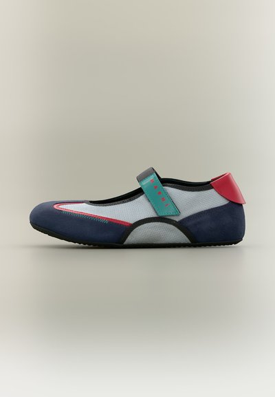 Chaussure plate Mary Jane avec bout et talon bleu marine, côtés en mesh blanc, bride bleu sarcelle avec texte rouge, et languette de talon rouge.