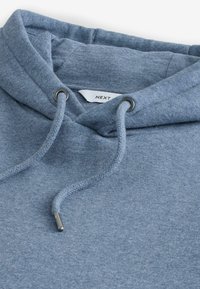 Felpa blu con cappuccio e lacci metallici, che mostra il cappuccio piegato e l'etichetta del marchio "NEXT" visibile all'interno del colletto.