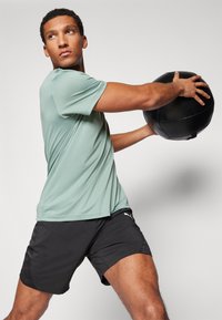 Conjunto deportivo que cuenta con una camiseta de manga corta verde claro y pantalones cortos negros. La camiseta tiene una textura suave y los pantalones cortos incluyen acentos de panel lateral.