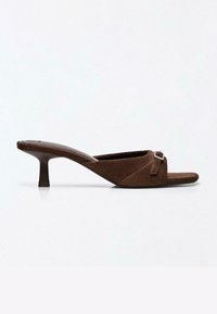 Mule en daim marron à bout ouvert avec un talon kitten de hauteur moyenne et une bride décorative avec boucle, présenté en profil latéral sur fond blanc.