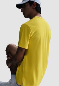 Camiseta deportiva amarilla hecha de un tejido suave y que absorbe la humedad. Mangas cortas, cuello redondo y aberturas laterales para mayor facilidad de movimiento.