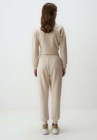 Beige sweatshirt en joggers, van zacht materiaal, met een relaxte pasvorm. Joggers hebben een elastische tailleband en boorden, gecombineerd met witte en tan sneakers.