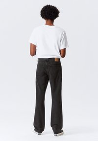 Jeans in denim nero slavato con taglio a gamba dritta e tasche posteriori. Abbinati a una t-shirt bianca semplice a maniche corte.