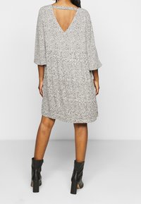 Mustat ja valkoiset kukkakuosiset mekko, lyhythihainen, V-mallinen selkäosa ja gathered vyötärö, yhdistetty mustiin nilkkureihin.