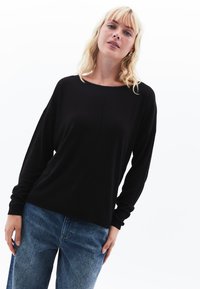 Maglietta nera a maniche lunghe con scollatura ampia e taglio morbido. Tessuto morbido con una consistenza liscia, abbinata a jeans azzurri.