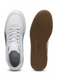 Zapatillas deportivas blancas con diseño de punta perforada, acentos en gris, cuello acolchado, cordones planos y suela de goma marrón texturizada con un dibujo en relieve.