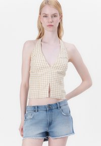 Top corto de halter a rayas beige y blancas con un escote en V profundo y una abertura frontal, combinado con pantalones cortos de mezclilla desgastados con bordes deshilachados.