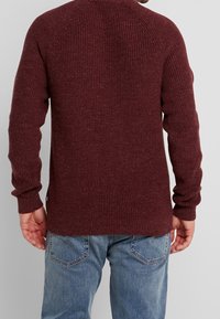 Merlotinpunainen neulepaita, jossa on resorikuvioitu pinta, pitkät hihat ja pyöristetty helma. Yhdistetty vaaleansinisiin farkkuihin, jotka näyttävät rentoilta.