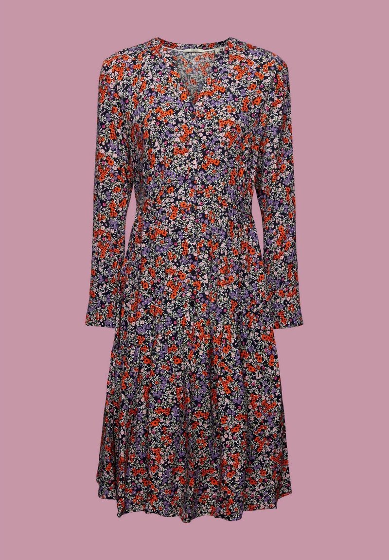 Pitkähihainen mekko, jossa on purppuran, punaisen ja valkoisen kukkakuosin, V-pääntie, tukeva vyötärö ja lantioon laskeutuva helma vaaleanpunaisella taustalla.