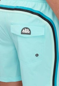 Costumi da bagno azzurri chiari con una tasca posteriore che presenta una toppa logo nera, accentuati da strisce laterali nere e turchesi. Texture liscia.