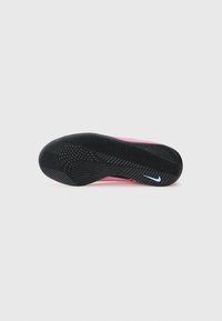 Svart teksturert såle av en rosa Nike-sko med hvit swoosh-logo på en helt hvit bakgrunn.