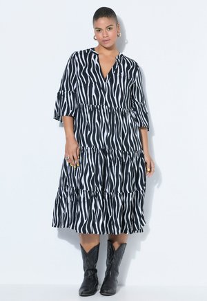 Kvinde står iført en sort og hvid zebra-stribet midikjole med trekvart-ærmer og sorte cowboystøvler.