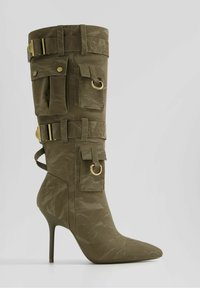 Olivgrön högklackad stövel med spetsig tå, strukturerat material, flera fickor, guldaccenter och en figursydd ankeldesign.