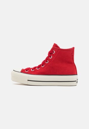 Sneaker alte rosse in suede con suola in gomma bianca, striscia nera decorativa e occhielli metallici per i lacci.