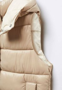 Beige Steppweste mit Kapuze, ausgestattet mit einer glänzenden, glatten Textur und vertikalen Nähten. Enthält Druckknöpfe und eine Fronttasche.