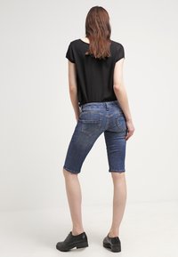 Džínové bermudy s tmavým praním, designem s pěti kapsami a přiléhavým střihem, kombinované s černým krátkým topem a černými botami.