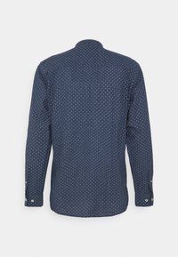 Long-sleeve shirt in dark navy with small white polka dots, collared neck, button cuffs, and a smooth, textured fabric.