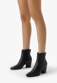 Czarne skórzane botki za kostkę z ostrym noskiem, średnim obcasem blokowym i zapięciem na zamek błyskawiczny z boku. Gładka tekstura, minimalistyczny design.