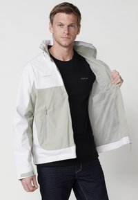 Une veste légère bicolore en gris clair et blanc, dotée d'une capuche, de poches zippées et d'une doublure en mesh. Matériau résistant avec une finition lisse.