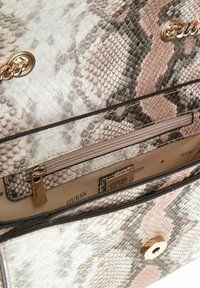 Intérieur d'un sac à main designer en cuir imprimé serpent montrant une poche zippée, une étiquette logo Guess, et un détail de chaîne dorée.