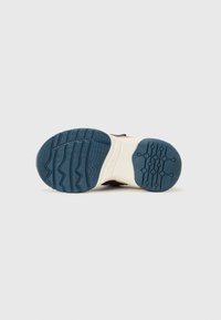 Schuhsohle aus strukturiertem blauen Gummi mit Zickzackmuster, geschwungenen Kanten und einer cremefarbenen Zwischensohle mit Branding an der Seite.