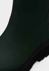 Donkergroene rubberlaars met zwarte zool, gladde textuur en elastisch zijpaneel voor gemakkelijk aan- en uittrekken.