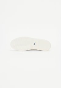 White shoe sole with a textured, grooved surface for grip. Features a rectangular blue tag embedded near the heel. Smooth, matte finish.