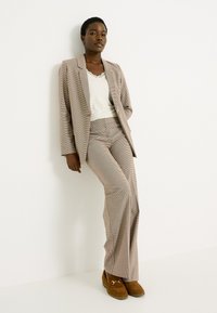 Costume à motif en nuances de beige, rouge et bleu ; blazer ajusté avec revers et pantalon évasé assorti ; top crème en dessous ; chaussures marron.