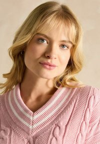 Hele roosa kudumine sviiter, mis sisaldab nööridesse kudumise mustrit, v-kaelusega koos valgete triipudega, tekstuuriga kangast ja soonikkoes detailidega.