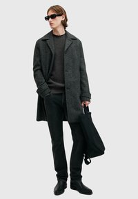Szary, teksturowany płaszcz z klasycznym kołnierzem, noszony na ciemnym swetrze i czarnych dżinsach. Czarna torba na ramię i eleganckie czarne buty dopełniają stylizację.