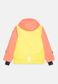 Barnens vattentäta jacka med gul baksida, korallfärgade ärmar och huva, svarta handledsmuddar och reflexpatch nära fållen.