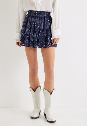 Navy ruffled skirt featuring a paisley pattern, with a fitted waistband. Paired with white cowboy boots with decorative stitching.