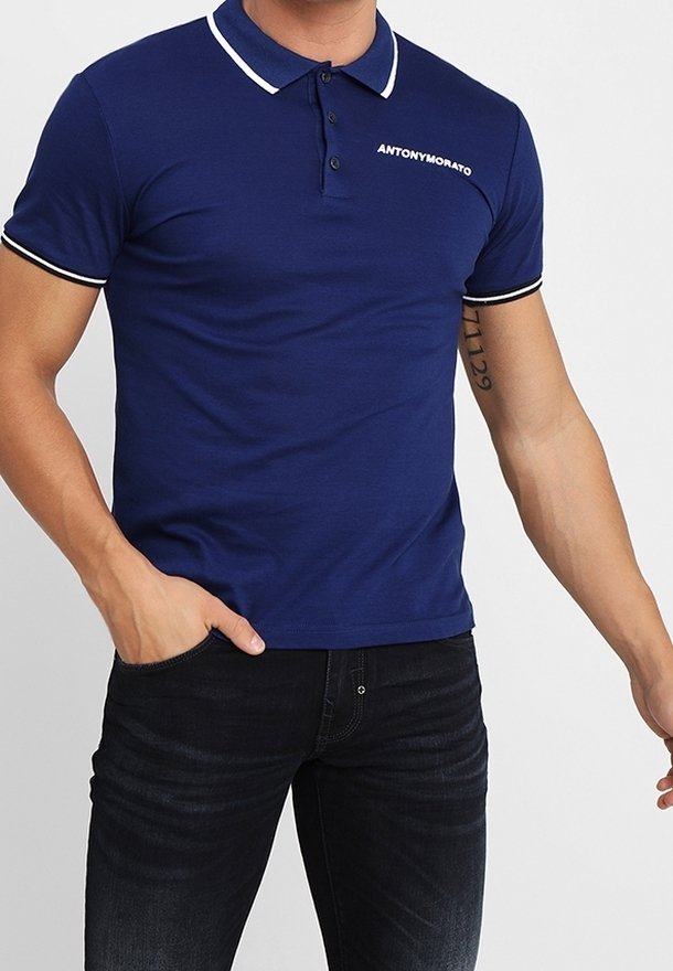 Polo bleu marine avec col et accents de manche blancs, doté d'une patte de boutonnage à trois boutons et d'un détail logo sur la poitrine. Texture de tissu lisse.