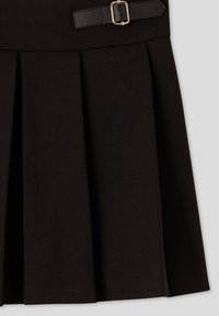 Sezione di gonna nera plissettata con una cintura in pelle nera e dettaglio in fibbia argentata in vita su uno sfondo grigio chiaro.