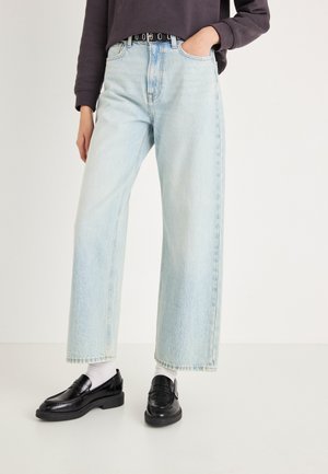 Jeans a gamba larga in denim color azzurro chiaro, con vita alta e finitura sbiadita. Abbinati a mocassini neri e calzini bianchi.