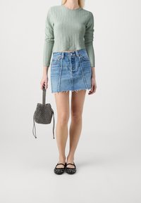 Minzgrüner strukturierter Pullover, blauer Denim-Minirock mit fransigem Saum, schwarze gemusterte Bucket-Bag und schwarze mit Nieten verzierte Ballerinas.
